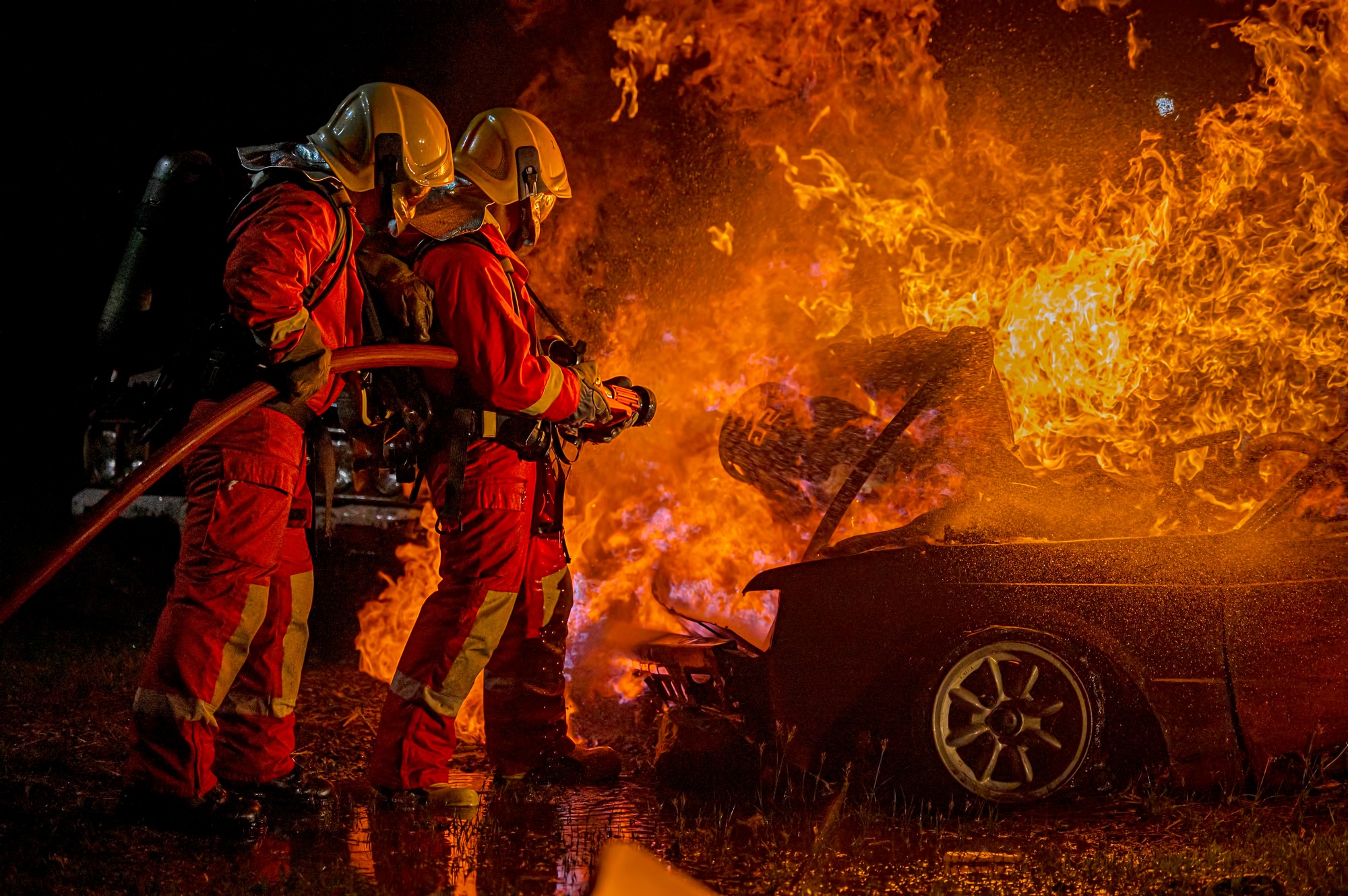 A firefighter in training sprays a burning car with a fire hose nozzle.